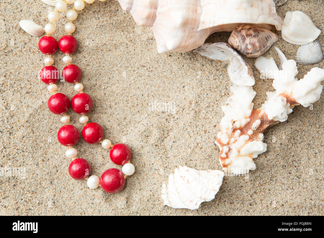 Muscheln und rote Halskette auf Sand am Strand Stockfoto