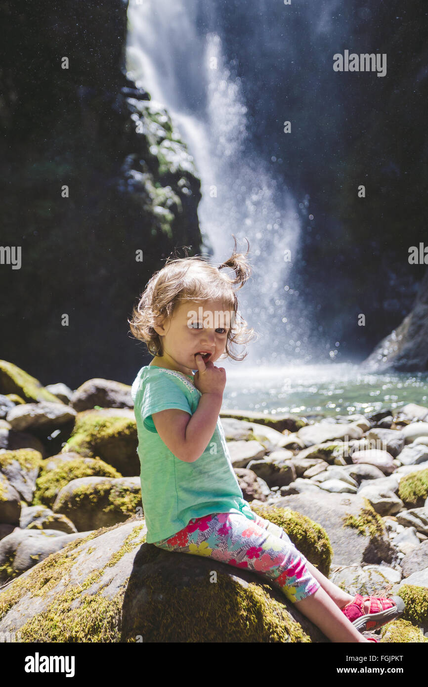 Junges Mädchen etwa 1,5 Jahre alt posieren für ein Porträt unter einem hohen Wasserfall im Umpqua National Forest in Oregon. Stockfoto