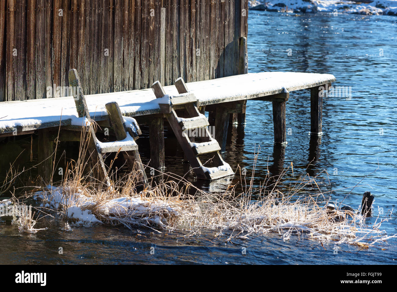 Zwei kleine hölzerne Stufen führen vom Baden und Angeln Brücke ins eiskalte Wasser neben einem Bootshaus im Winter. Einige Golde Stockfoto