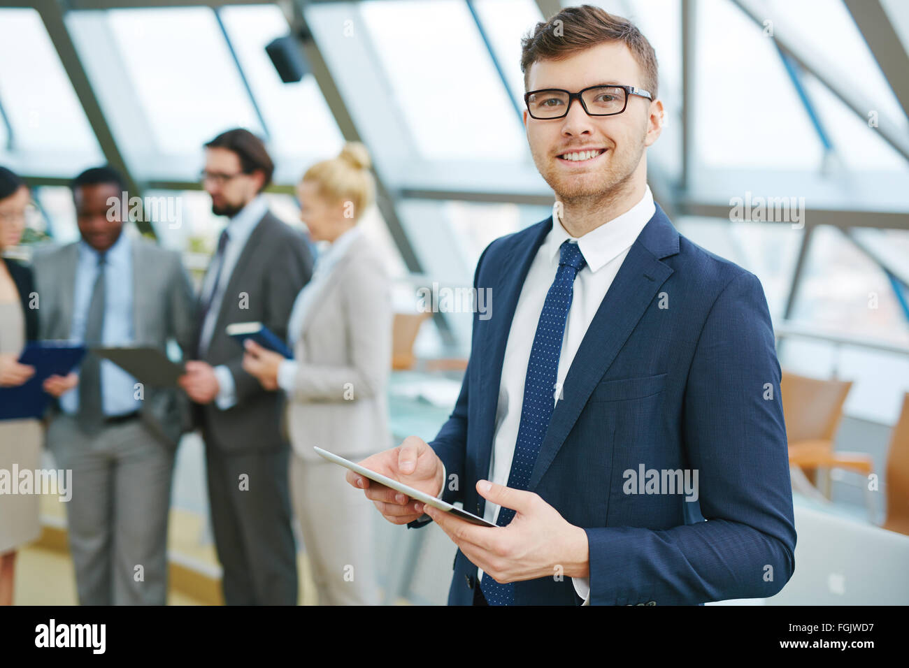 Junge Führungskraft mit Blick in die Kamera auf Grund der arbeitenden Bevölkerung touchpad Stockfoto