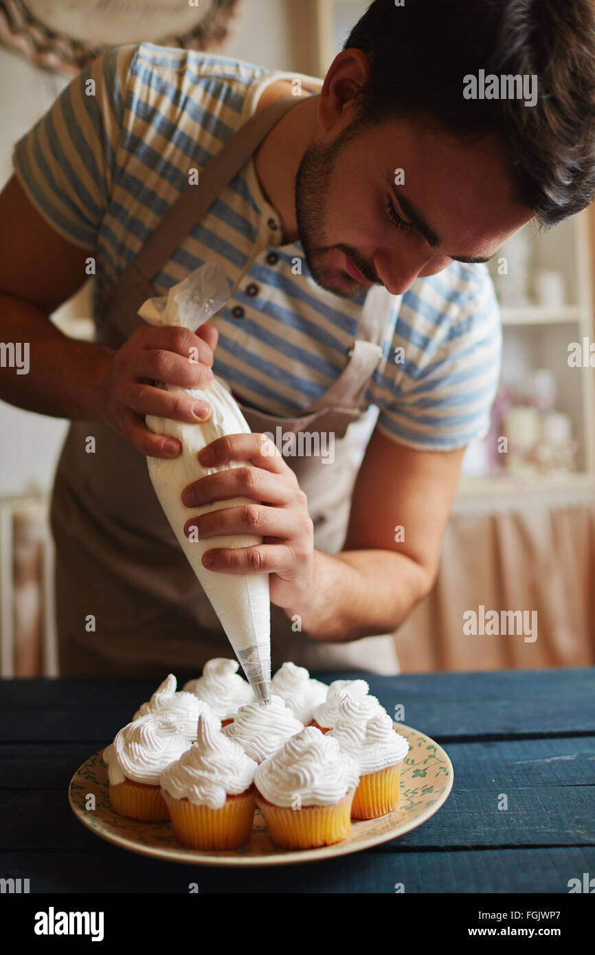 Baker, die Muffins mit weißer Sahne verzieren Stockfoto