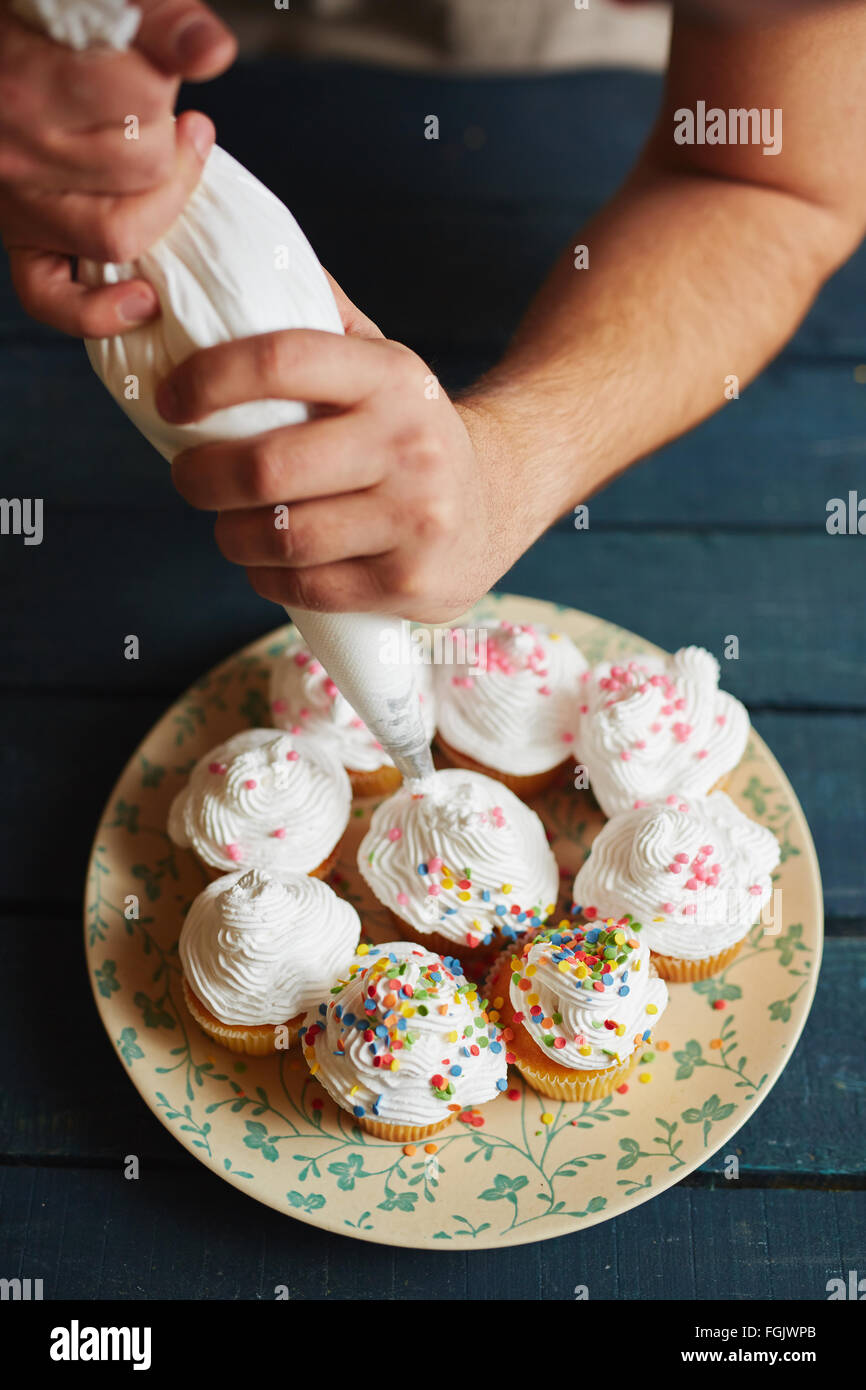 Hände des Bäckers Muffins mit Schlagsahne verzieren Stockfoto
