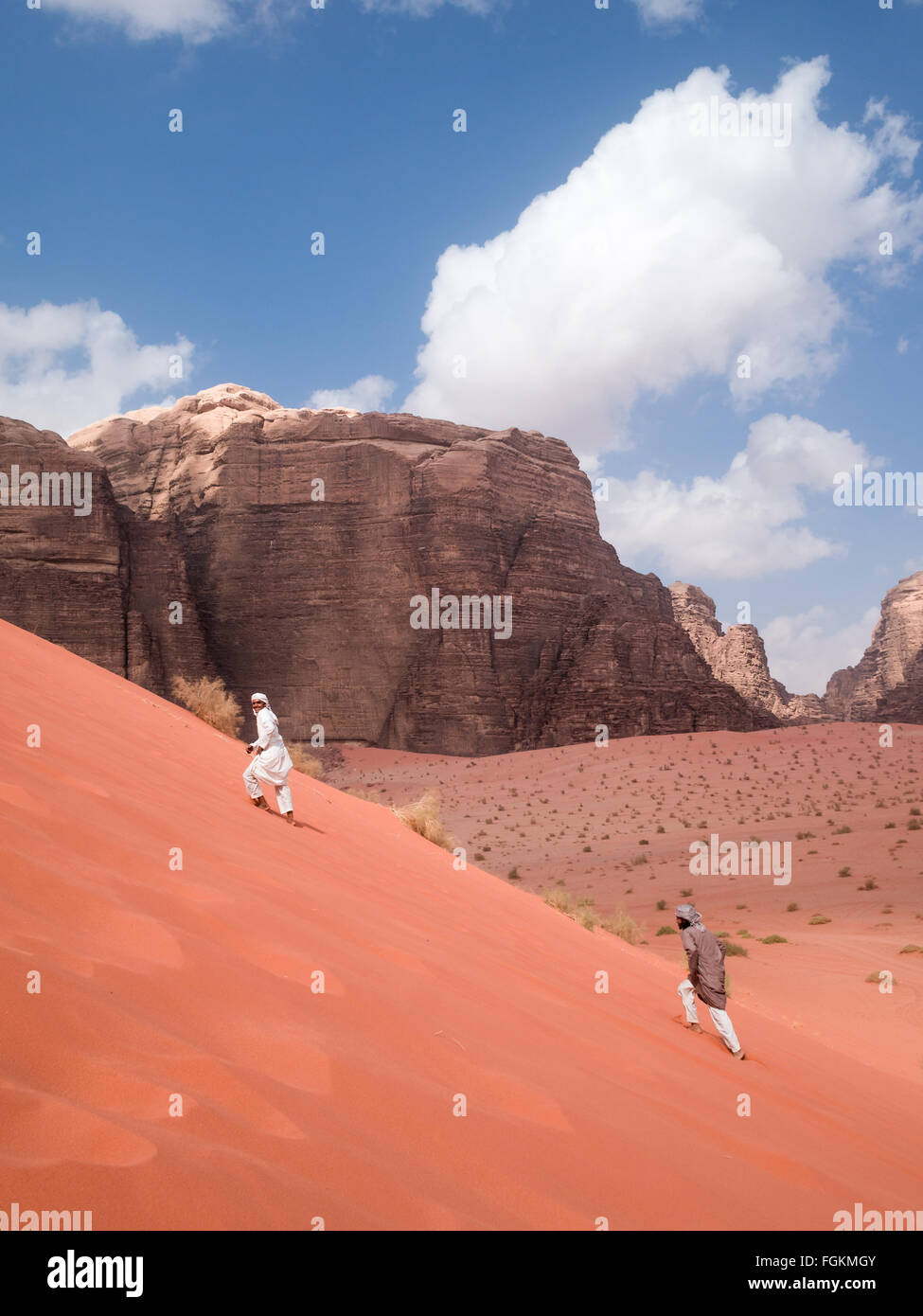 Zwei Männer, gekleidet in arabischer Tracht Aufstieg auf die roten Sanddünen der Wüste Wadi Rum Stockfoto