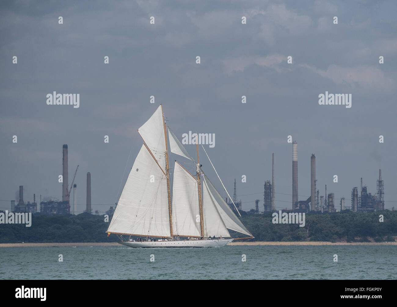 eine klassische Yacht mit zwei Masten in vollen weißen Segel Segel vorbei Fawley Kraftwerk an einem sonnigen Tag auf dem Solent, UK Stockfoto