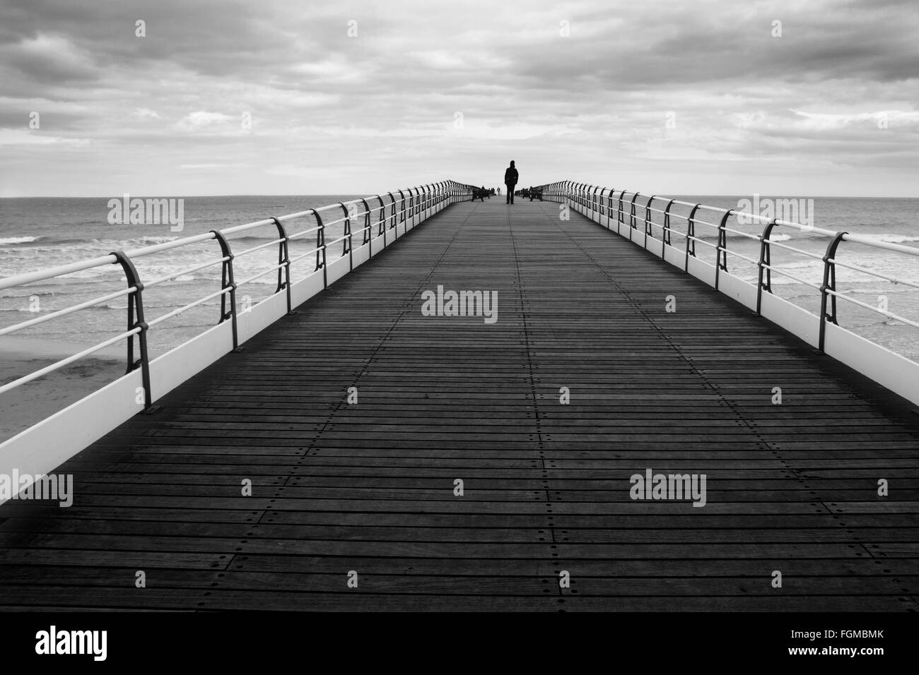 Ein monochromes Bild eine einsame Gestalt zu Fuß bis zum Ende des Saltburn Pier an der Ostküste von Cleveland, England Stockfoto