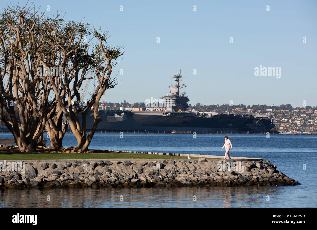 Frau zu Fuß in Tuna Harbor Park mit USS Carl Vinson im Hintergrund, San Diego, Kalifornien Stockfoto