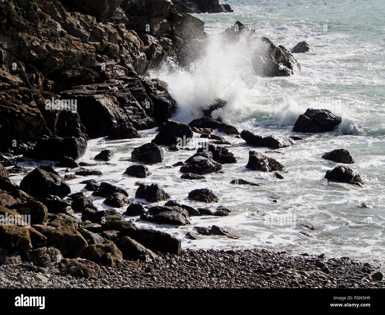 Wellen auf Felsen in Petit Bot Schach, Guernsey mit erodierten und abgestuften Geröllfelder auf den felsigen distance. Stockfoto