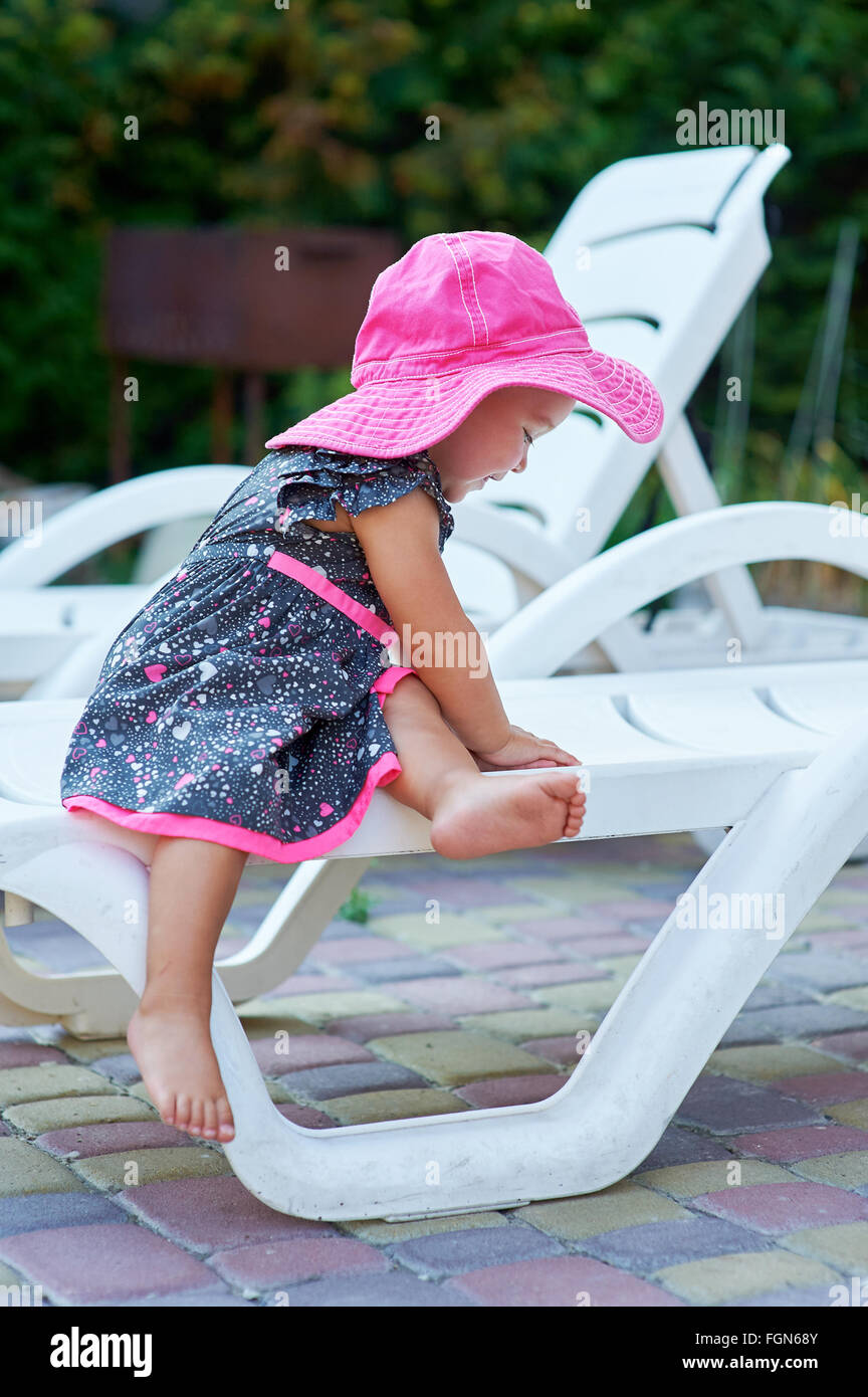 kleines Mädchen in einem roten Hut sitzt auf einer Liege Stockfoto