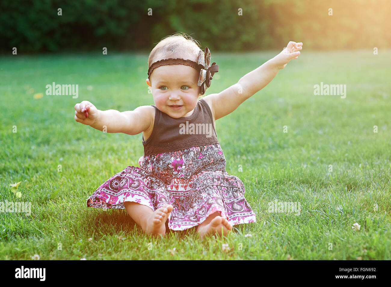 kleines Mädchen sitzt auf dem grünen Rasen auf dem Rasen Stockfoto