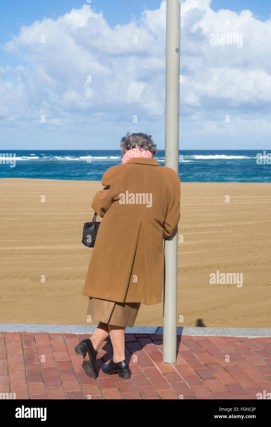 Ältere Frau stützte sich auf post mit Blick auf Strand und Meer. Stockfoto