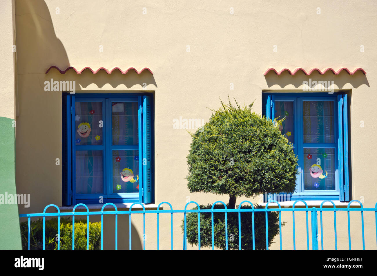 Zwei blaue Fenster in alten Haus verziert mit Kindern Gesicht Aufkleber von der blauen Metallzaun und Zierpflanze Stockfoto