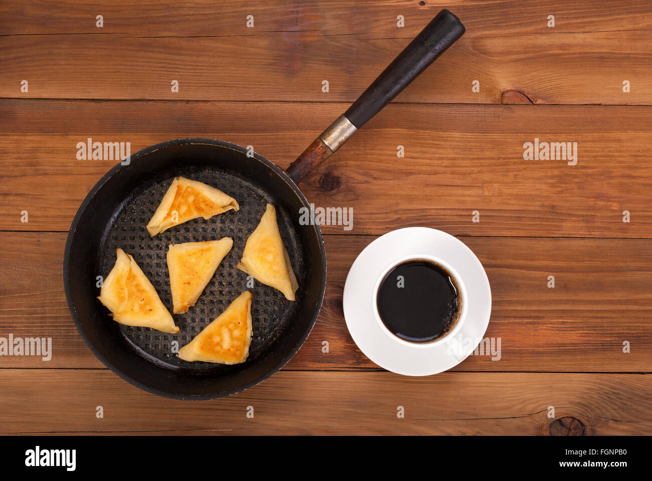 Fried-Pfannkuchen mit Füllung auf dem Teller und Kaffee auf einem Holztisch. Ansicht von oben. Stockfoto