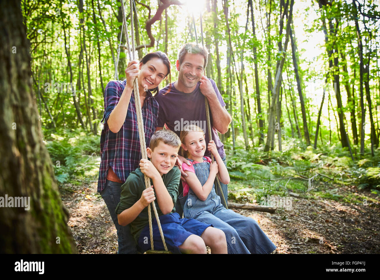 Lächelnde Familie Porträt am Seil schwingen im Wald Stockfoto