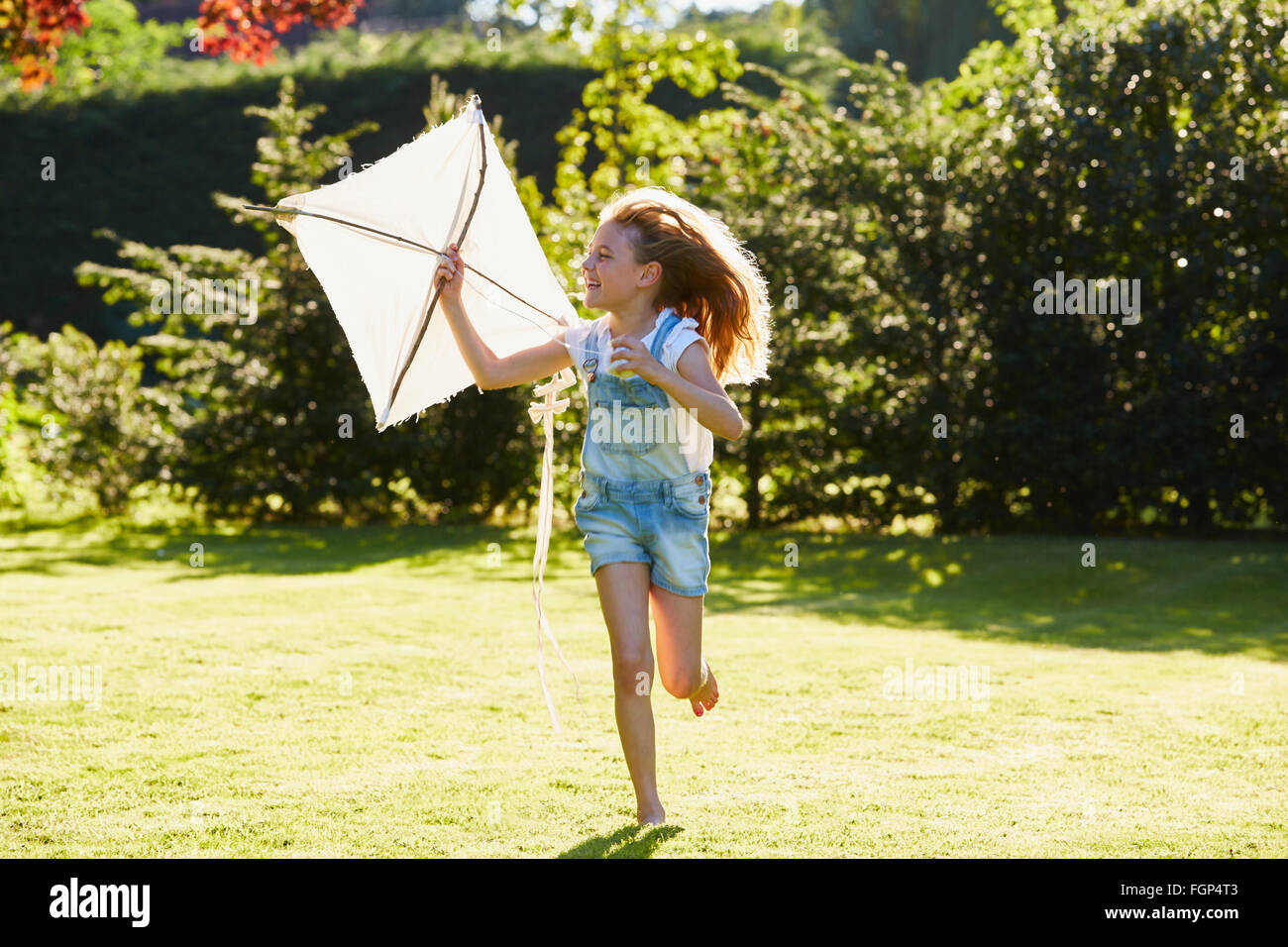 Mädchen mit Drachen im sonnigen Garten laufen Stockfoto