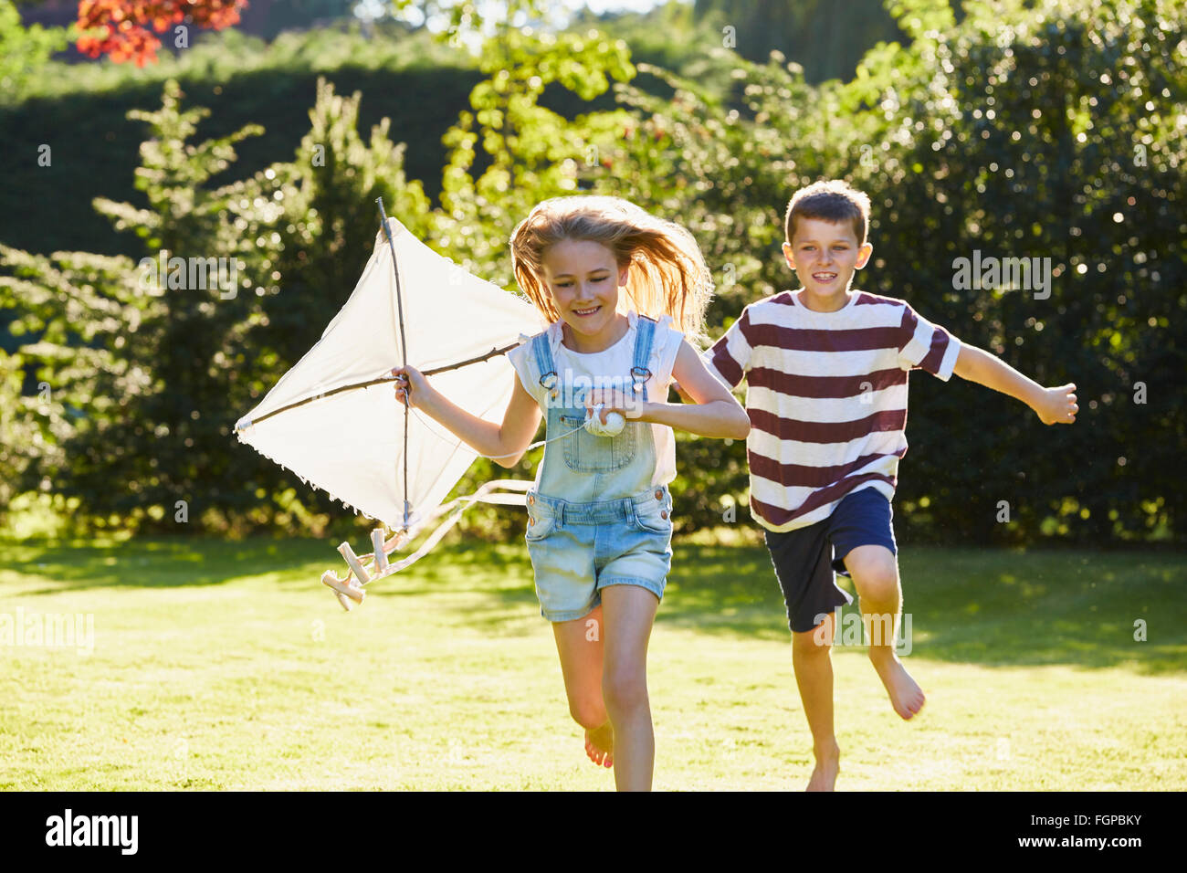 Bruder und Schwester laufen mit Drachen im sonnigen Garten Stockfoto