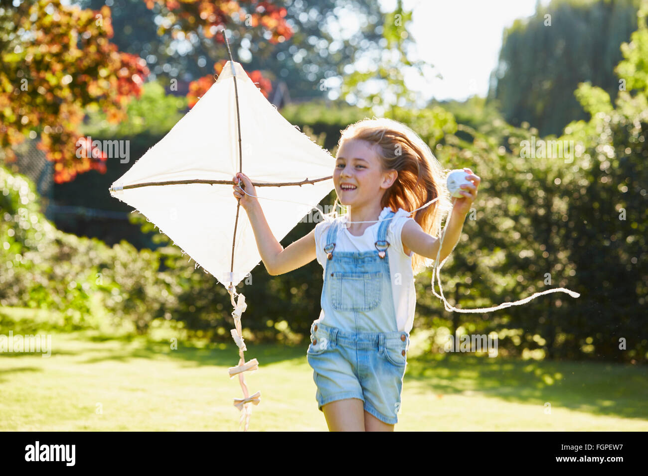 Begeisterte Mädchen laufen mit Drachen im sonnigen Garten Stockfoto