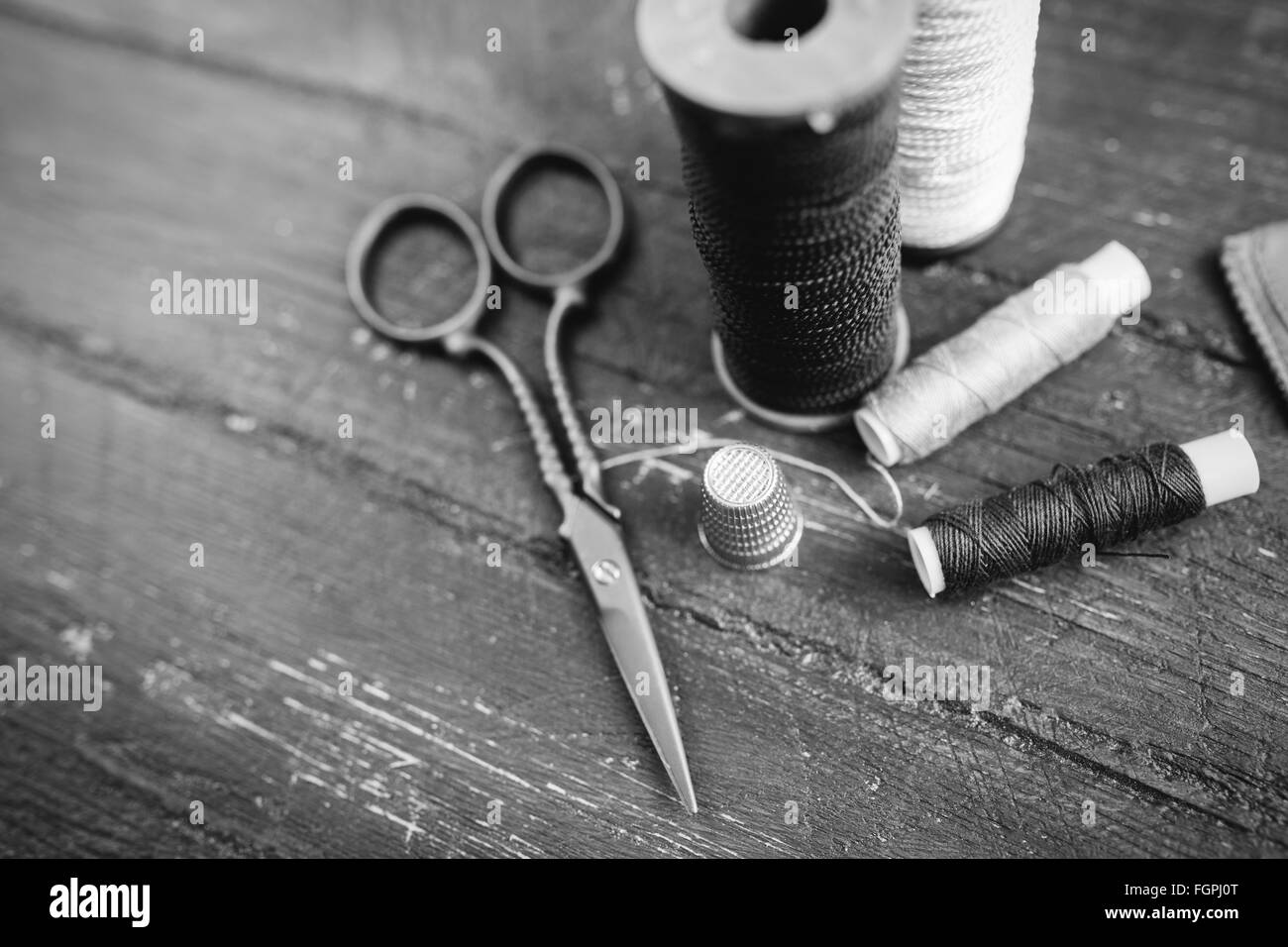 Nähen Zubehör: Spulen Faden, Schere, Nadel, Fingerhut auf Holztisch. Schwarz / weiß Foto. Schneidern und Nähen Konzept. Stockfoto
