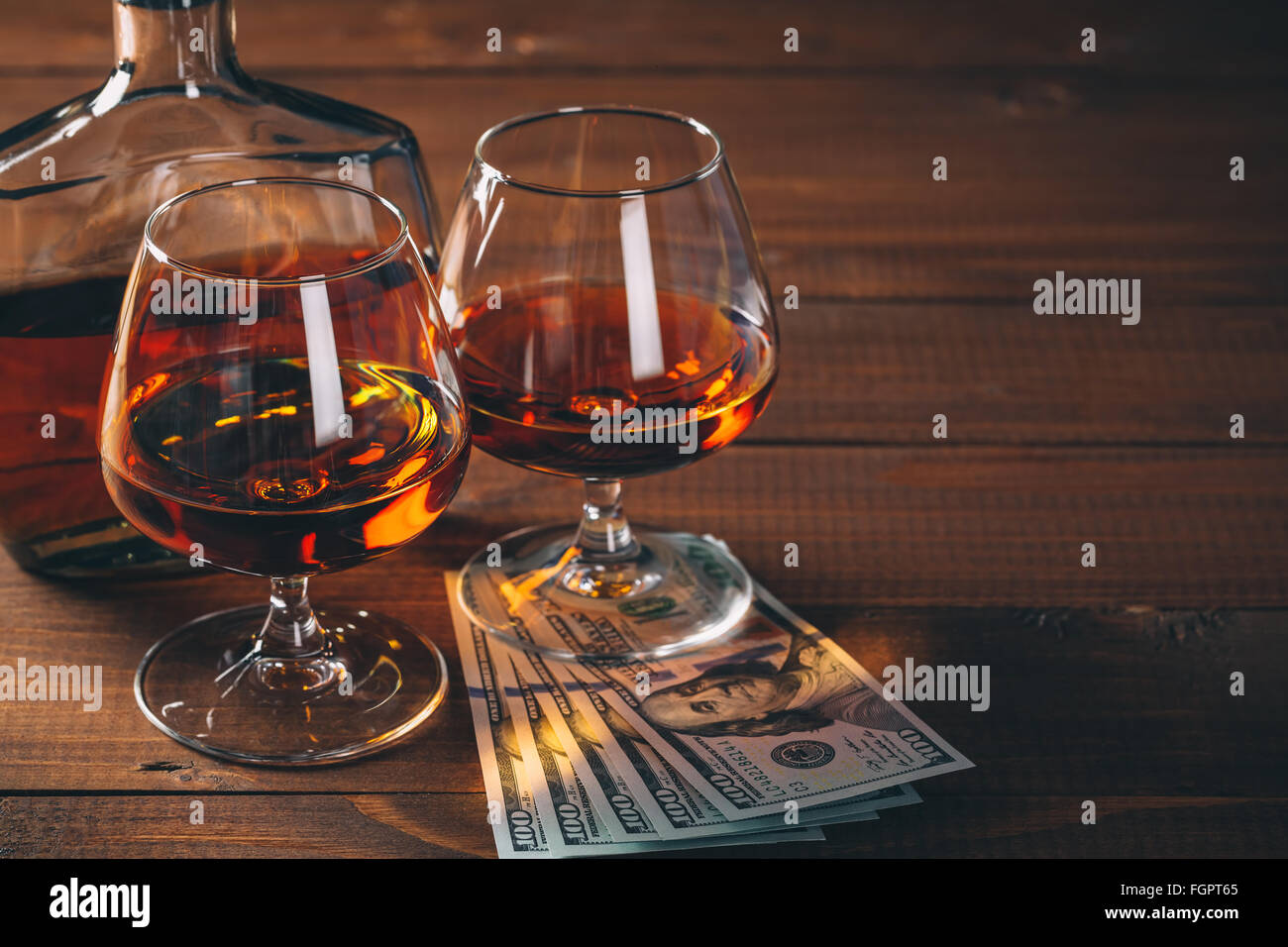 Zwei Gläser cognac und Flasche, mit Bündel Geld auf den Tisch. Stockfoto