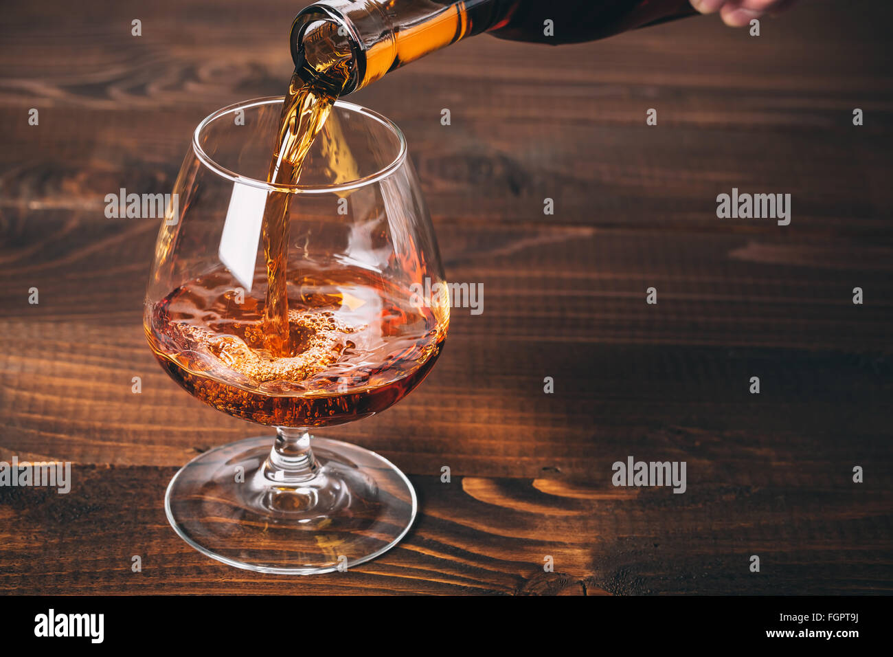 Gießt Cognac oder Whisky aus der Flasche in das Glas gegen Holz- Hintergrund Stockfoto