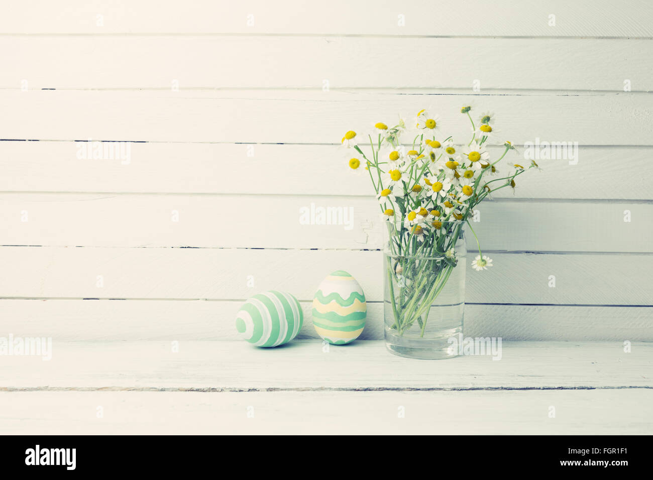 Bouquet von Kamillen ein Glas Vase und Ostern Eier in Pastellfarben auf weißer Holztisch Stockfoto