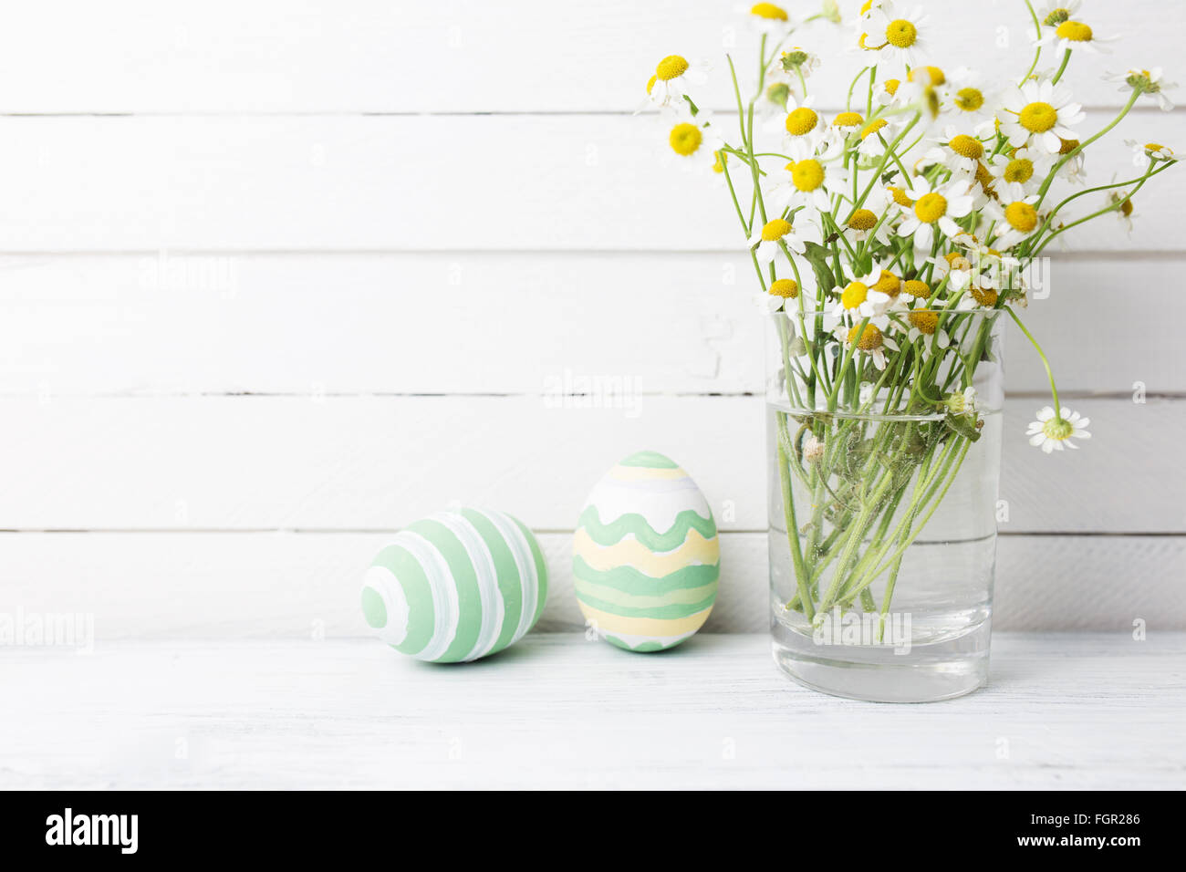 Bouquet von Kamillen ein Glas Vase und Ostern Eier in Pastellfarben auf weißer Holztisch Stockfoto