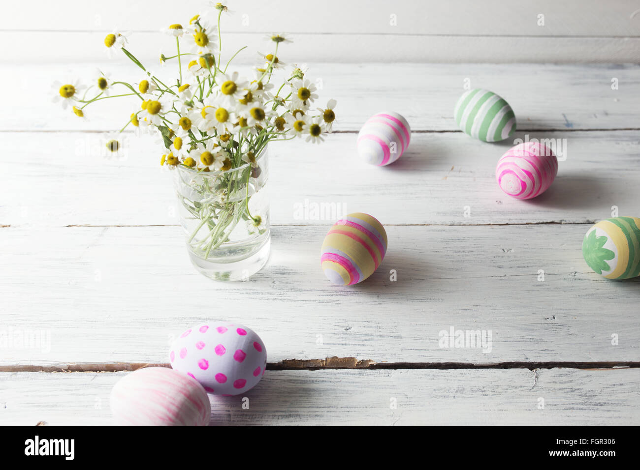 Bouquet von Kamillen ein Glas Vase und Ostern Eier in Pastellfarben auf weißer Holztisch Stockfoto