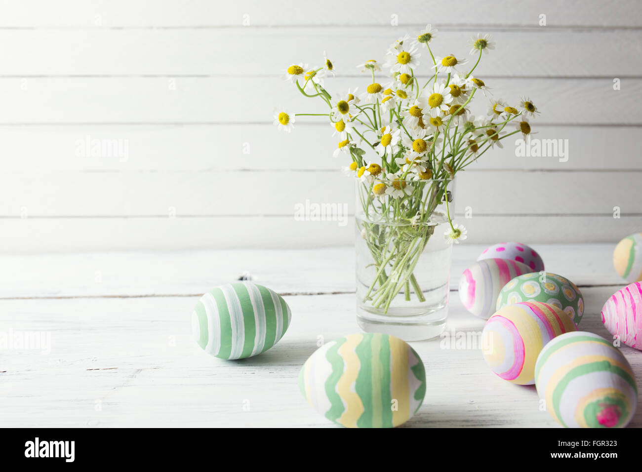 Bouquet von Kamillen ein Glas Vase und Ostern Eier in Pastellfarben auf weißer Holztisch Stockfoto