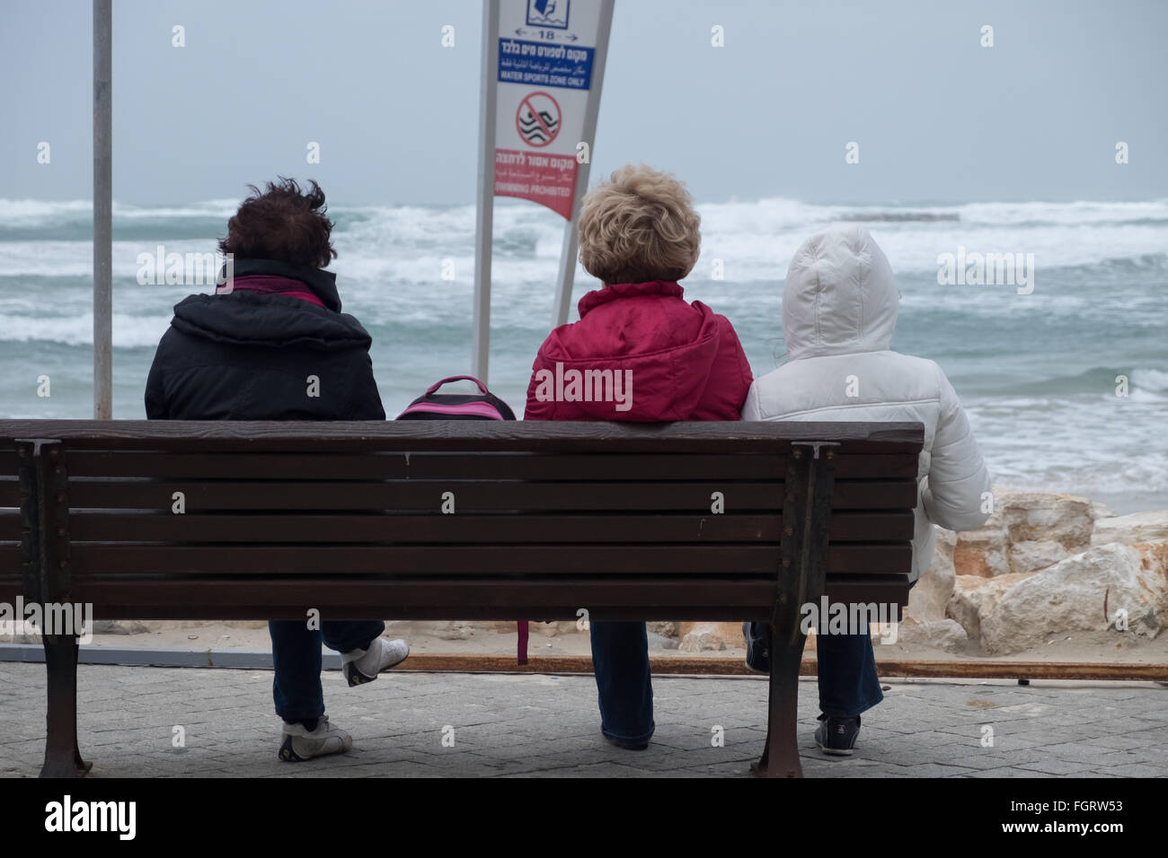 3 Frauen sitzen auf einer Bank an der Tel-Aviv-Promenade, Blick auf eine stürmische Mittelmeer an einem Wintermorgen Stockfoto