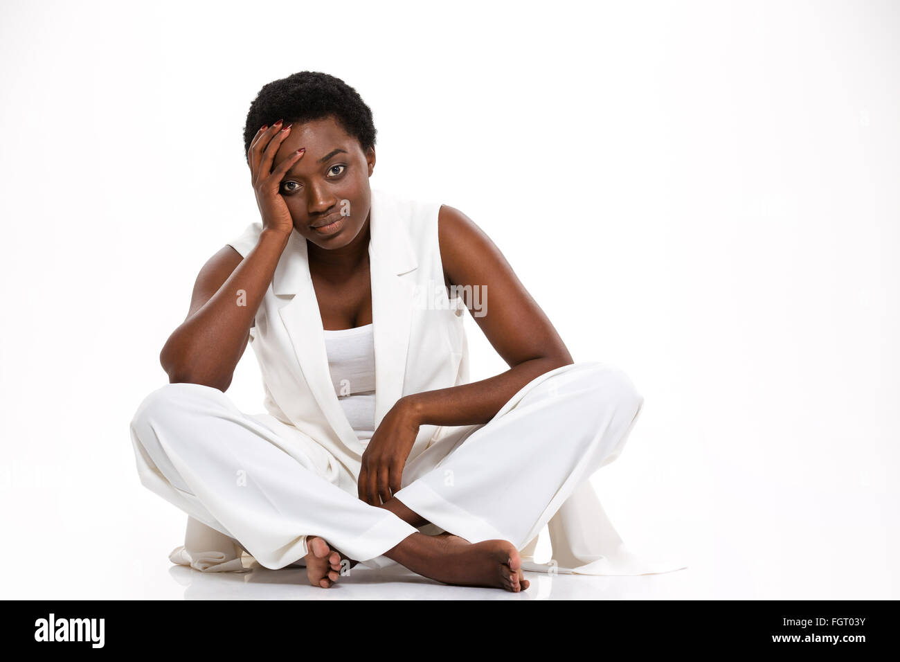 Müde, ziemlich afroamerikanische junge Frau sitzend mit Beine gekreuzt und mit Kopfschmerzen auf weißem Hintergrund Stockfoto