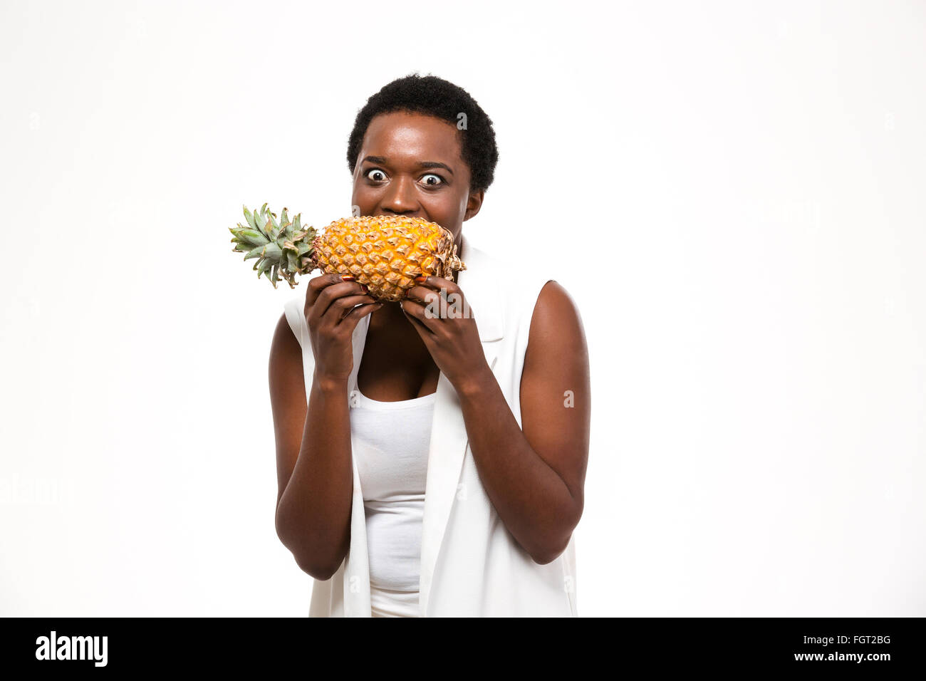 Hungrigen aufgeregt afroamerikanischen jungen Frau halten und beißen frischen Ananas auf weißem Hintergrund Stockfoto