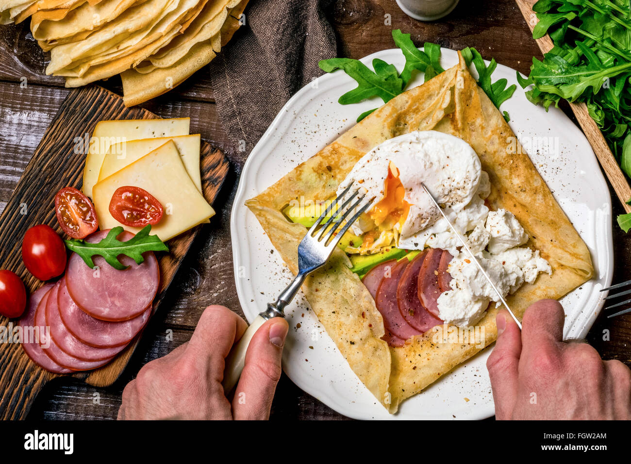 Mann isst Krepp Galette mit Fleisch, Avocado, weißer Käse und Spiegelei auf weißen Teller. Gesundes Frühstück Stockfoto