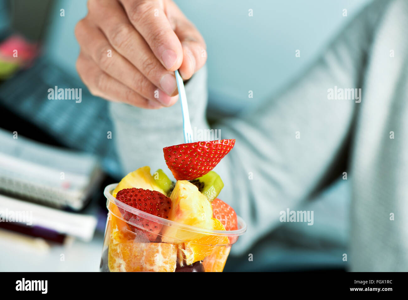 Closeup von einem kaukasischen Jüngling Essen einen Obstsalat aus einem klaren Plastikbecher im Büro Stockfoto