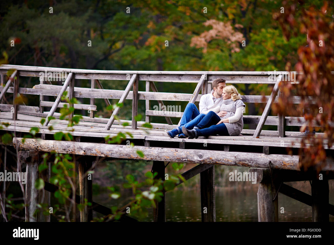 Mann küsst seine schwangere Frau sitzen auf einer Holzbrücke Stockfoto