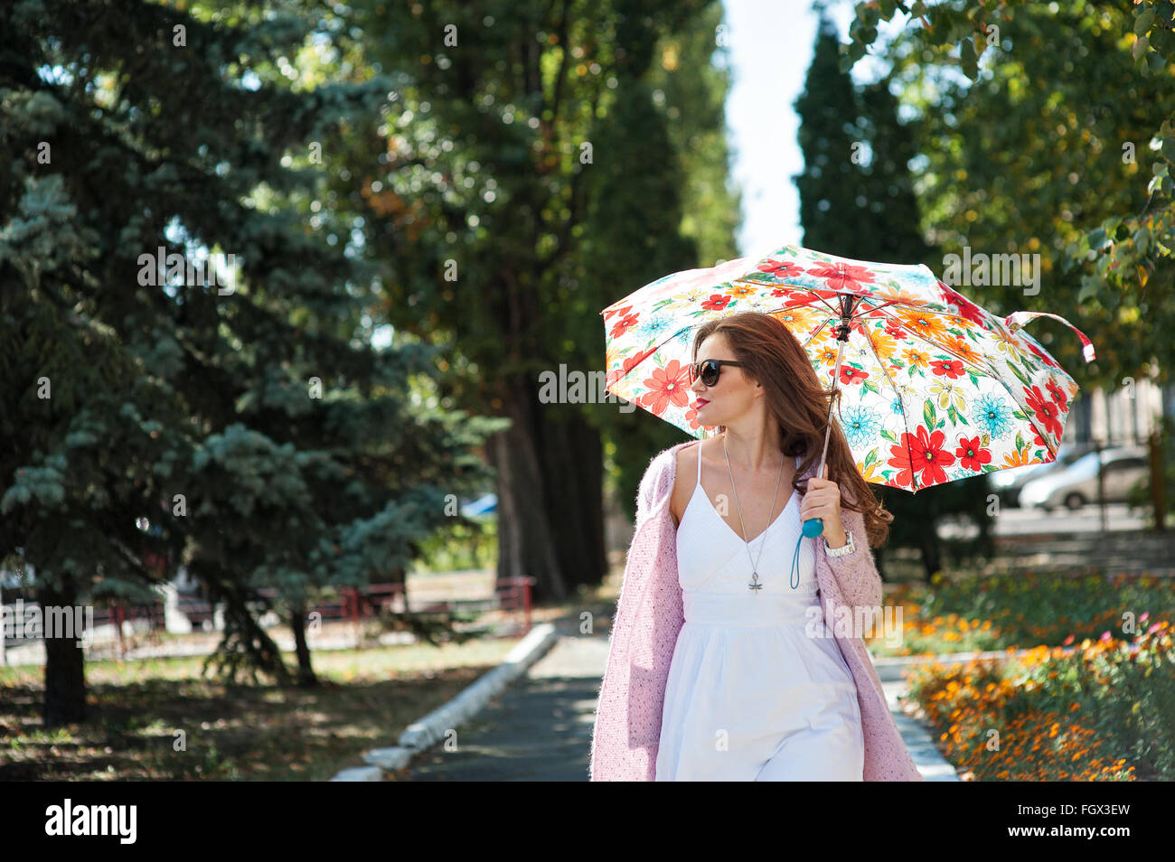 schöne Frau mit Sonnenbrille mit Regenschirm im Park spazieren Stockfoto