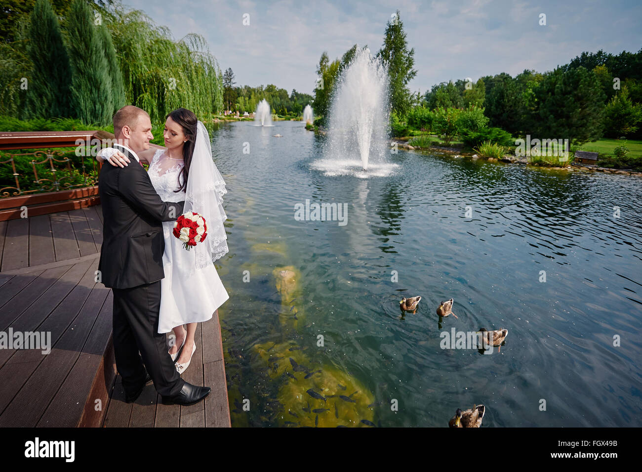 elegante stilvolle Bräutigam mit seiner glücklich wunderschöne Braut auf dem Hintergrund eines Sees mit Enten Stockfoto