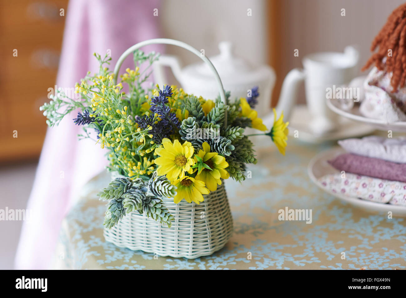 Bouquet von gelben Blüten in einem weißen geflochtenen Korb steht auf Holztisch Stockfoto