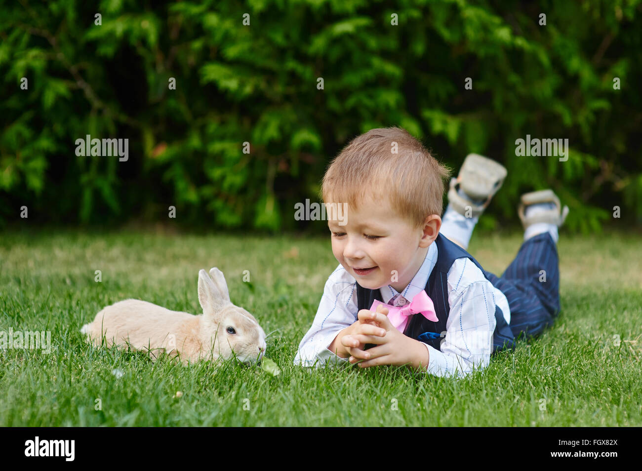 kleiner Junge spielt mit einem Hasen auf dem Rasen im park Stockfoto