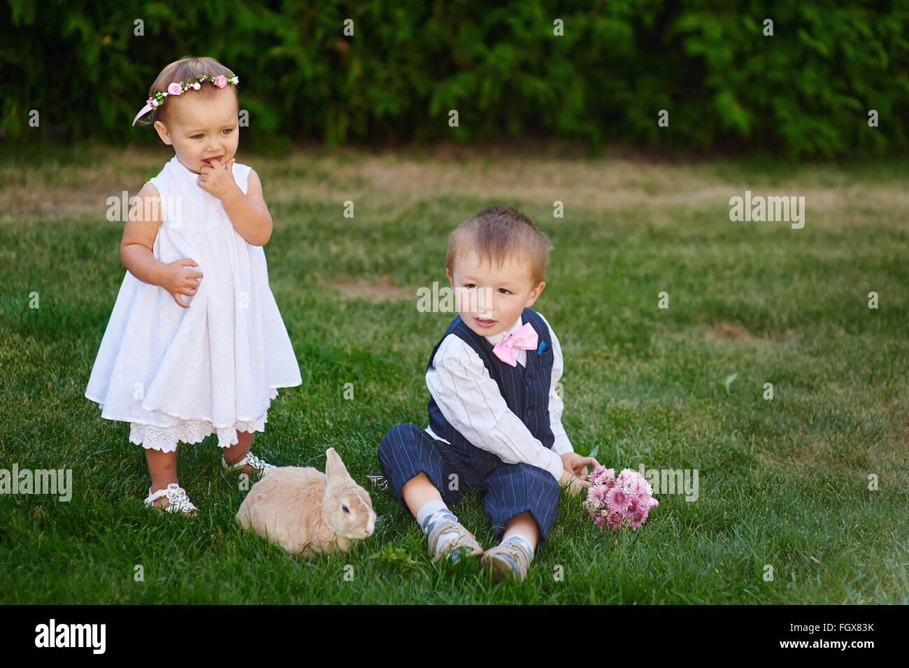 kleiner Junge mit dem Mädchen und Kaninchen spielen auf der Wiese Stockfoto