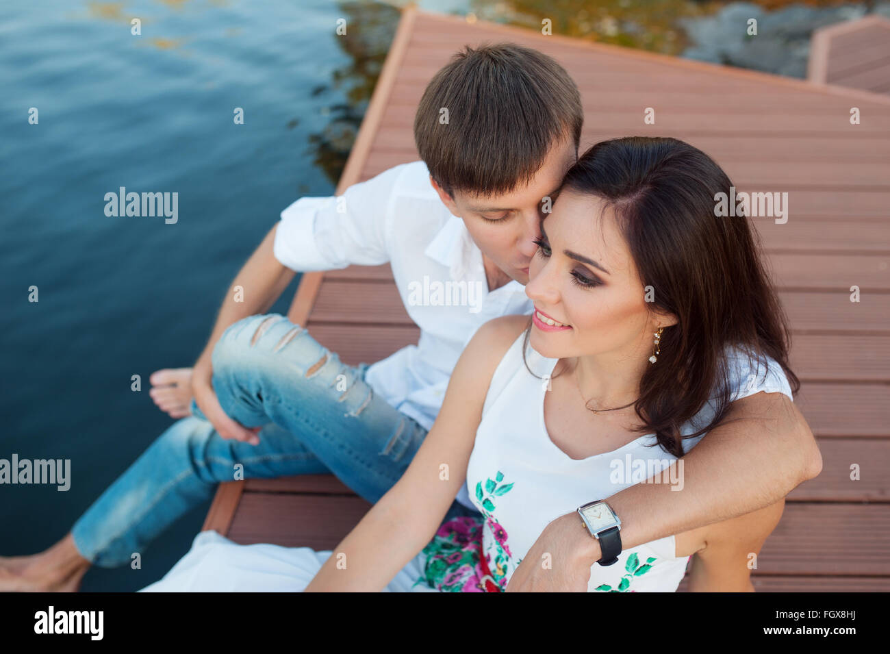 Mann umarmt Mädchen sitzen auf einem Pier am Ufer Flusses Stockfoto