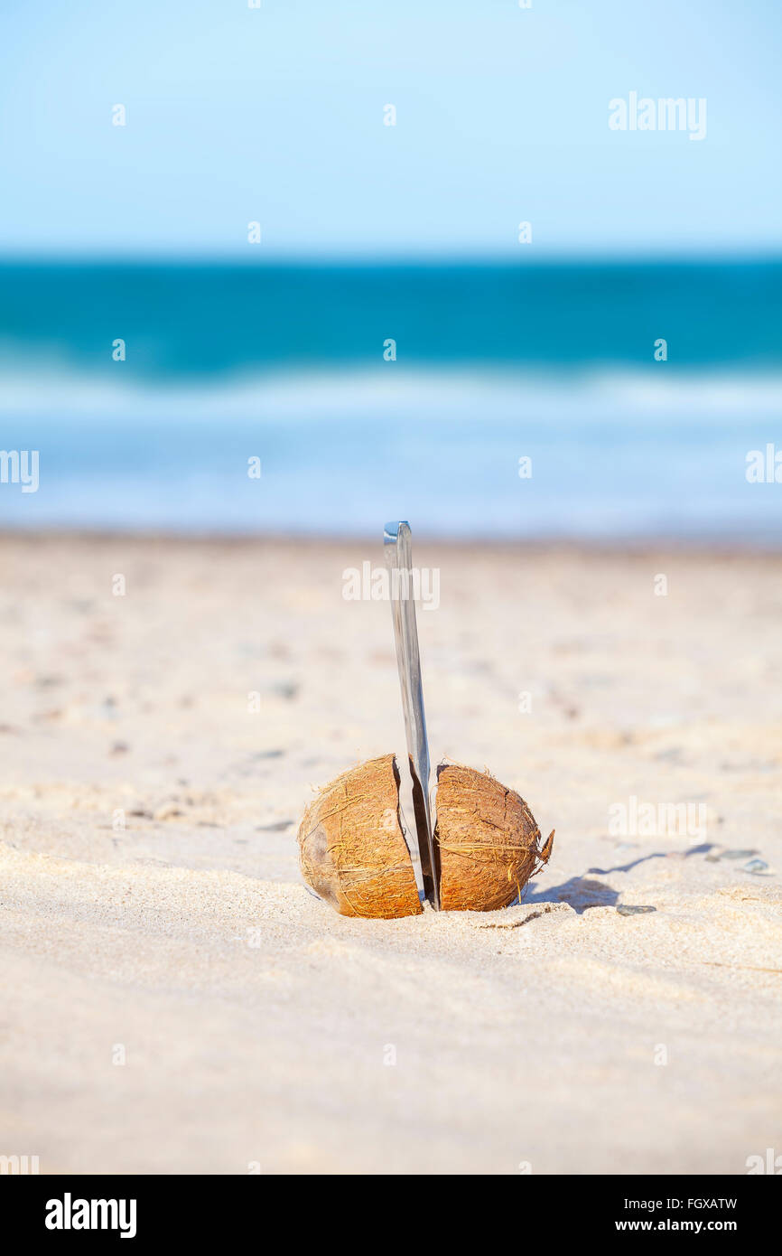Kokosnuss halbiert mit Messer an einem Strand. Stockfoto