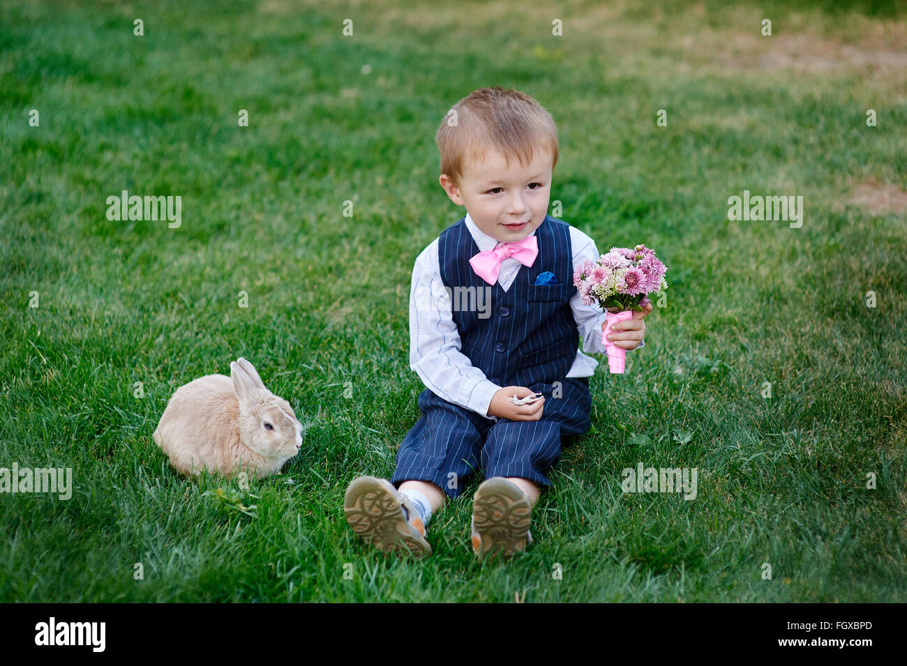 kleiner Junge mit einem Strauß Blumen und ein Kaninchen sitzen auf dem Rasen Stockfoto