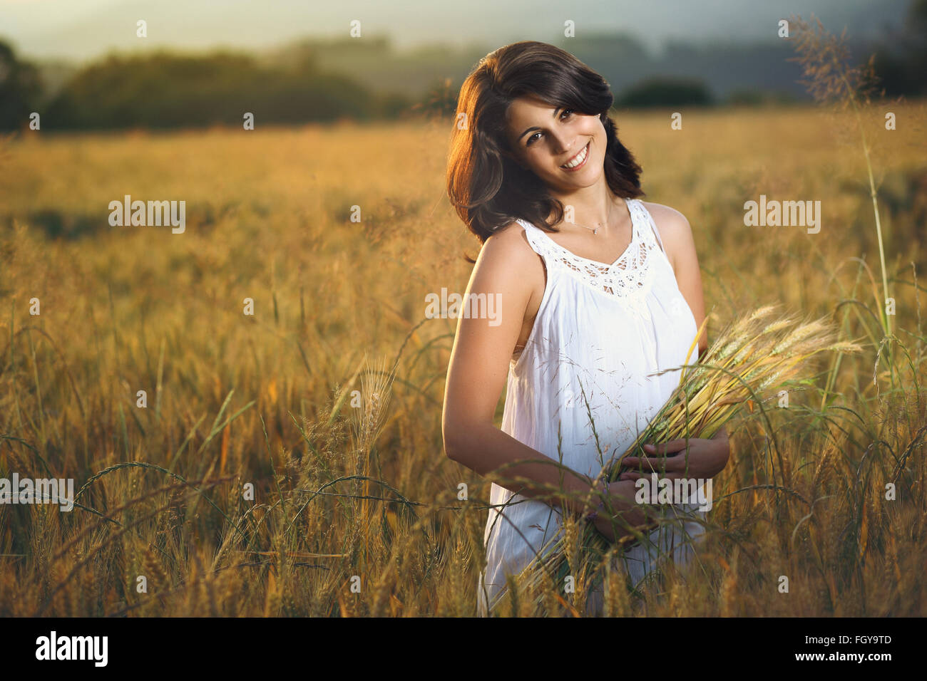 Wunderschöne lächelnde Frau in einem goldenen Feld bei Sonnenuntergang. Sommer-Saison-Porträt Stockfoto