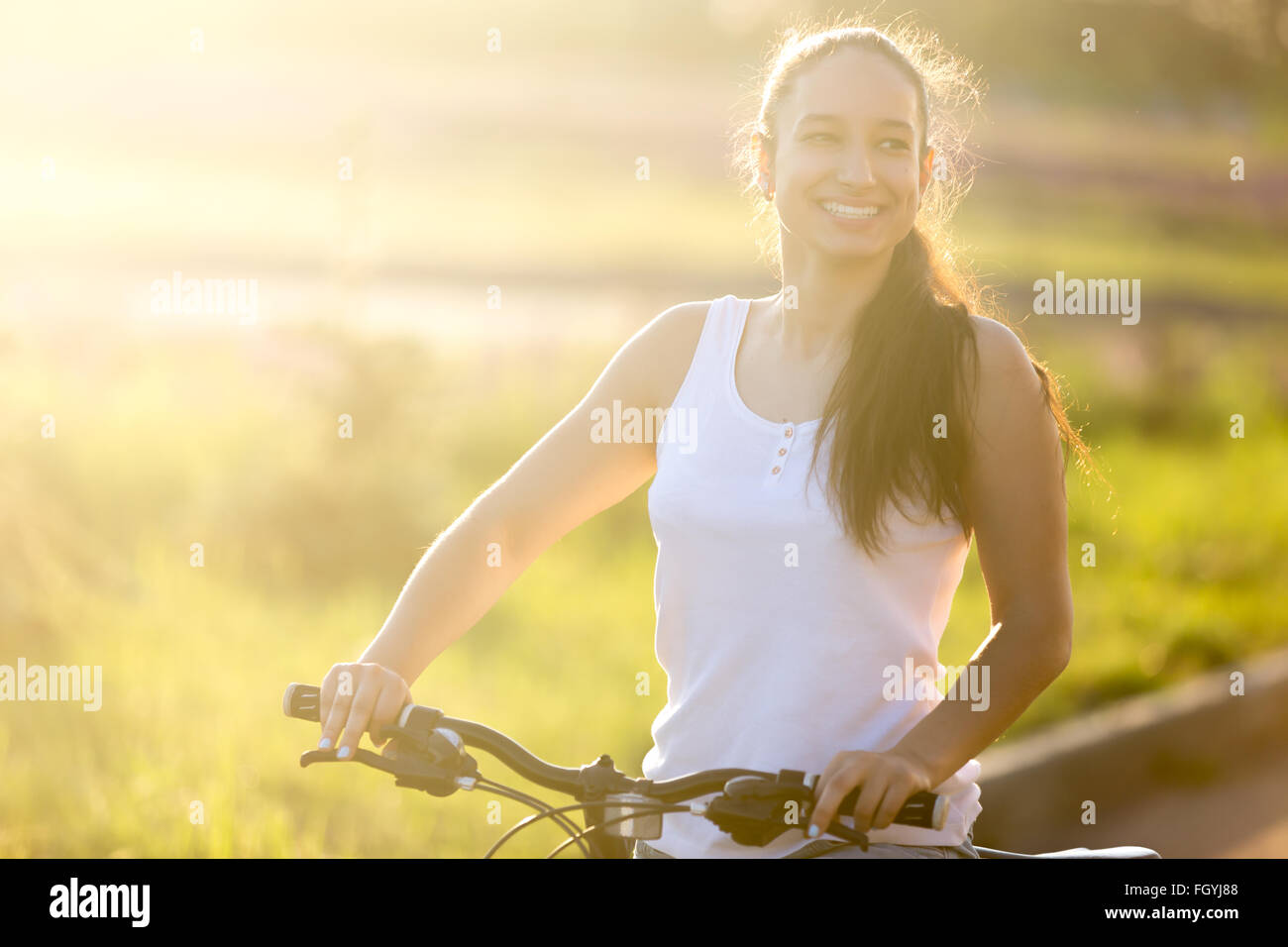 Porträt des Lachens junge asiatische-kaukasischen weiblichen Modells auf Fahrrad tragen legere Kleidung auf der Straße an hellen, sonnigen Sommertag Stockfoto