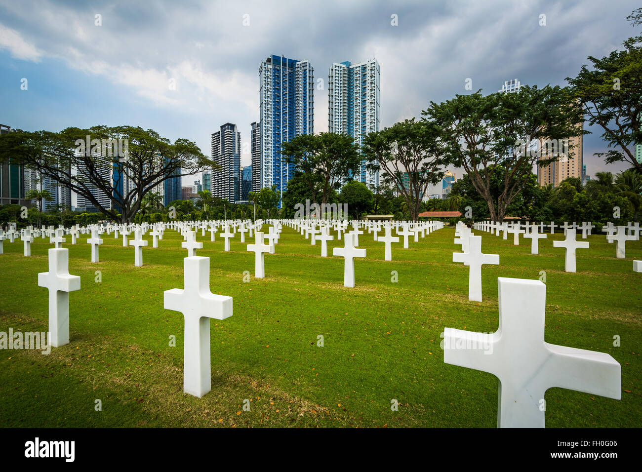 Gräber und moderne Gebäude in der Ferne am Manila American Cemetery & Denkmal in Taguig, Metro Manila, Philippinen Stockfoto