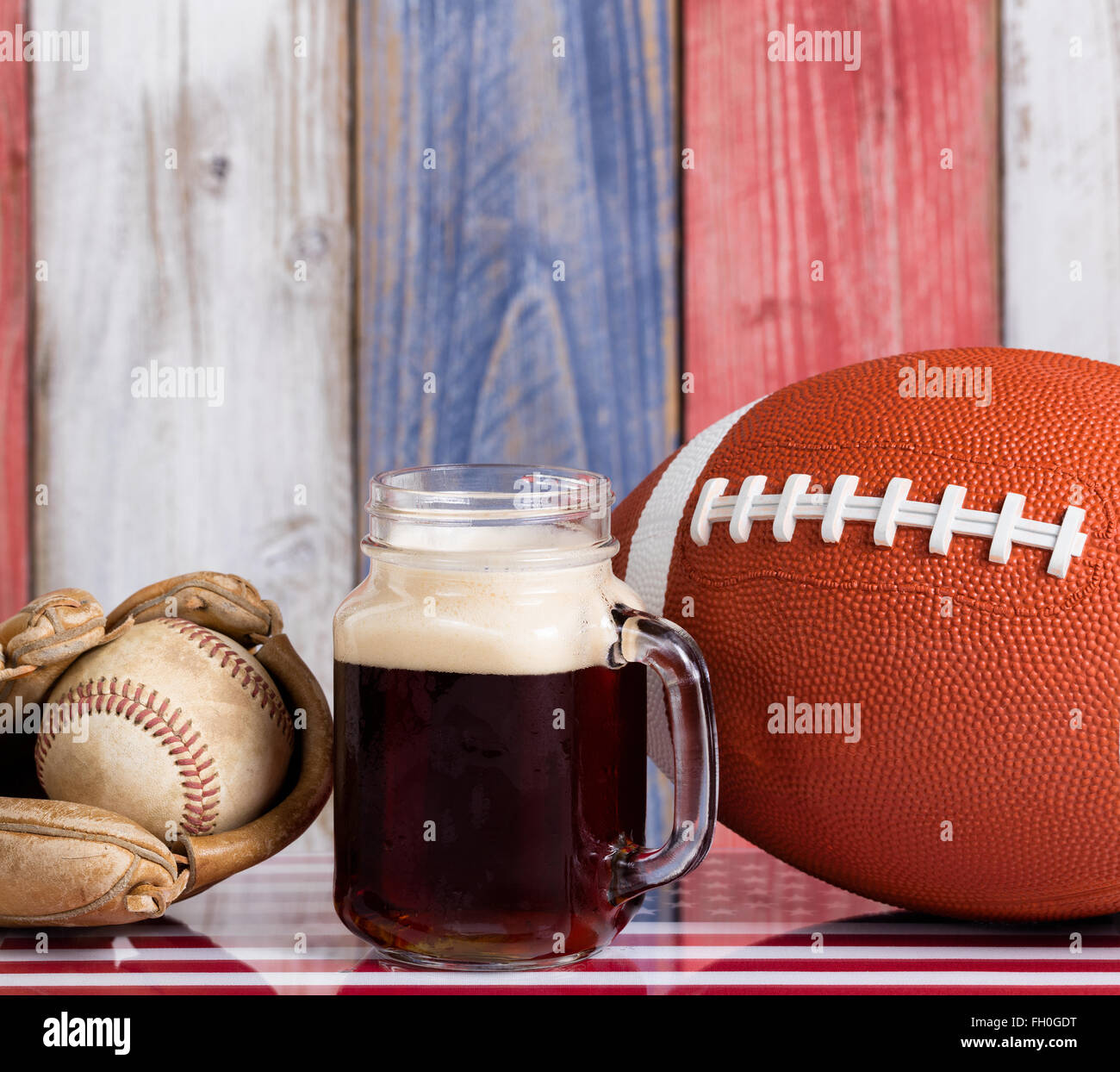 Schließen Sie nach vorne Blick auf ein Glas dunkles Bier mit einem abgenutzten Baseball Handschuh, Ball und Fußball. Stockfoto