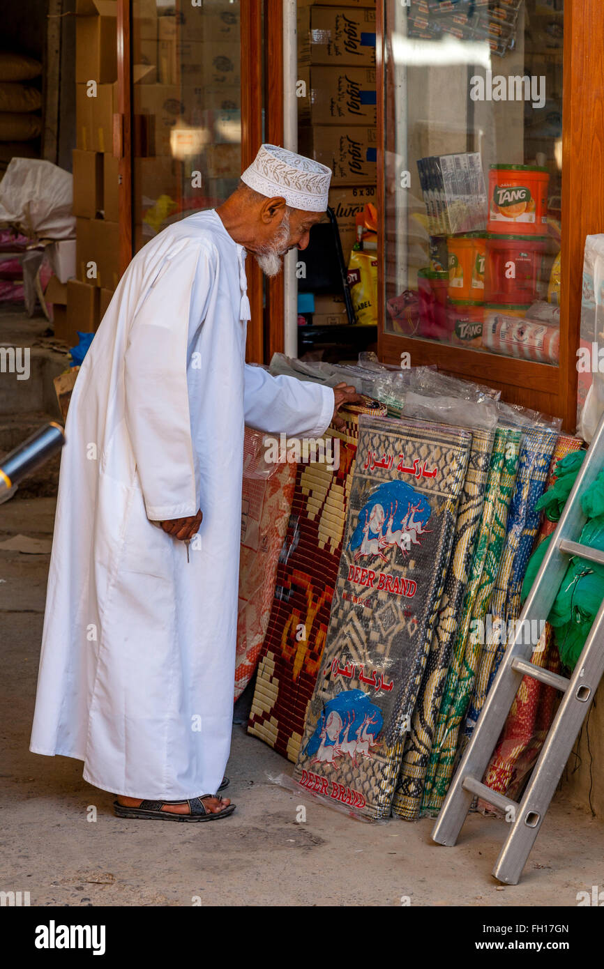 Ein älterer omanischen Mann suchen für Teppiche/Teppiche In The Nizwa Souk, Nizwa, Ad Dakhiliyah Region, Oman Stockfoto