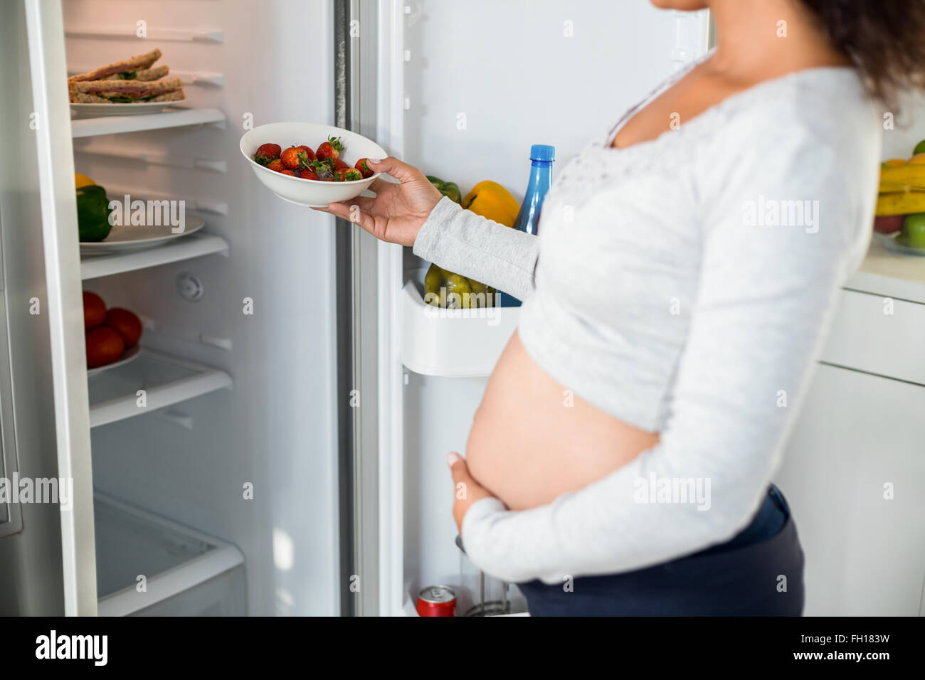 Schwangere Frau Erdbeeren im Kühlschrank zu halten Stockfoto