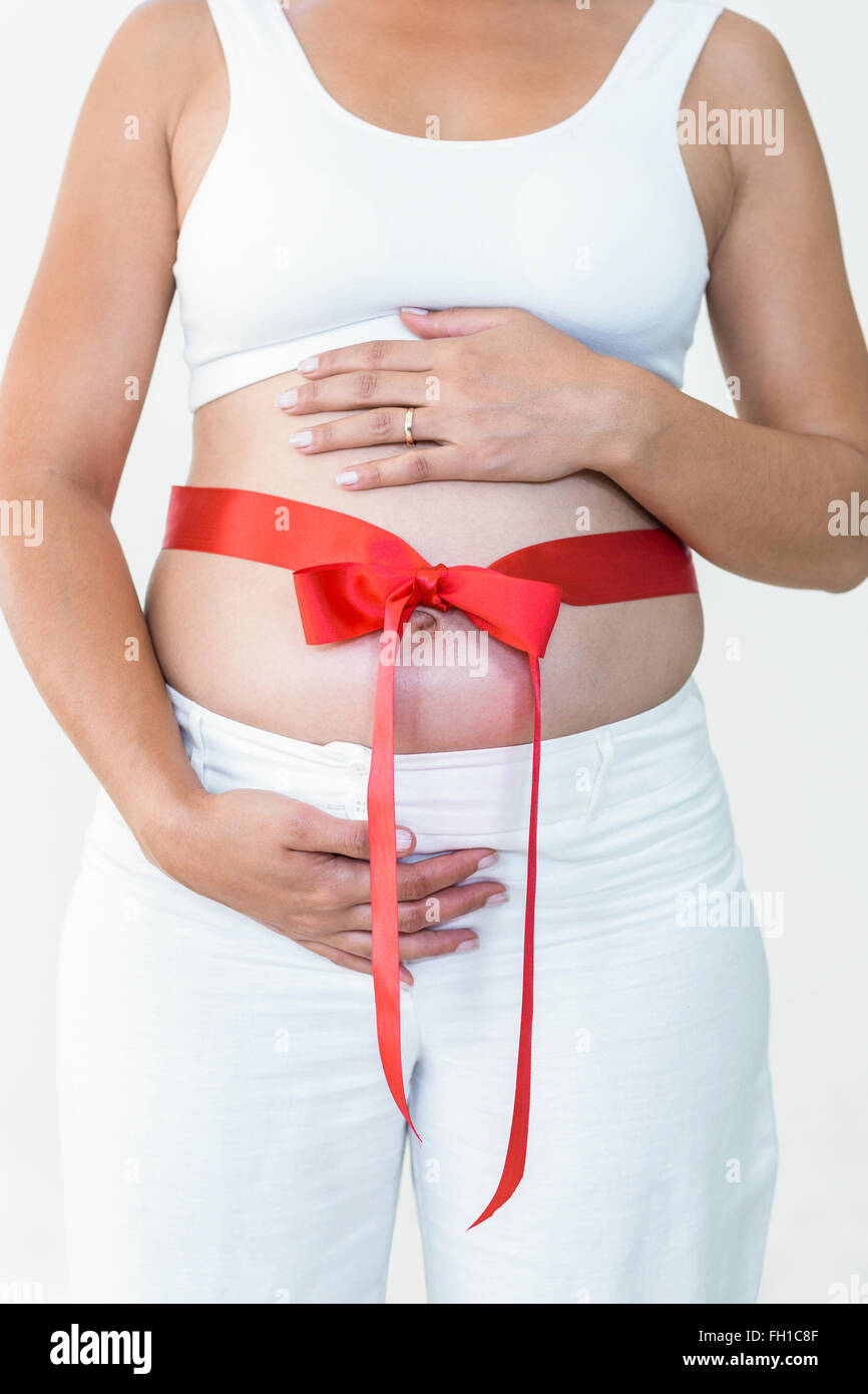 Mittelteil der schwangeren Frau mit einem roten Band um ihr Bauch Stockfoto