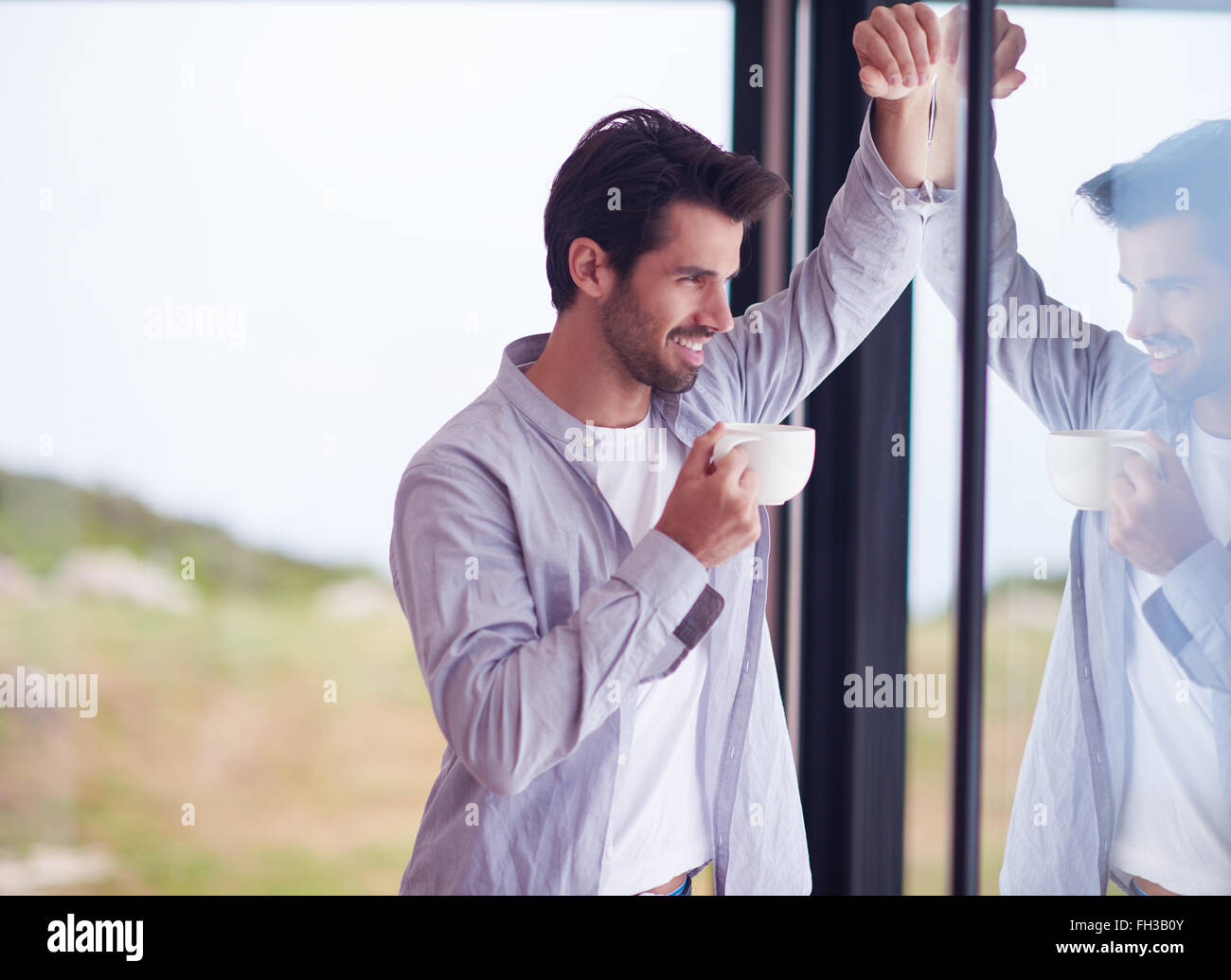 entspannte junger Mann trinken am ersten Morgen Kaffee Flaschen auf Fenster Regentropfen Stockfoto