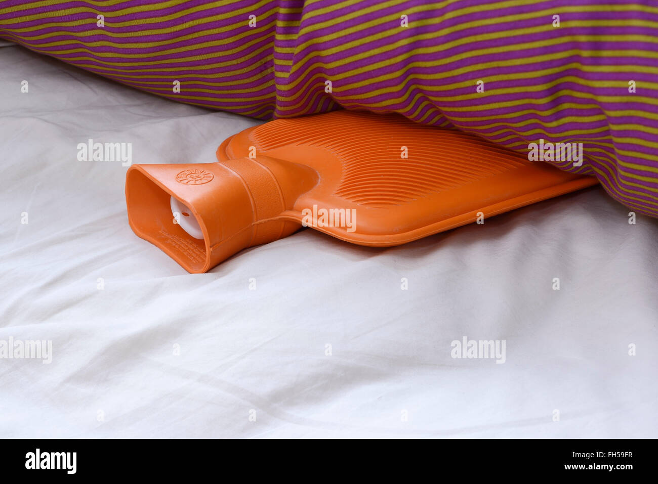 Eine orange Gummi-Wärmflasche in einem Bett liegend Stockfoto